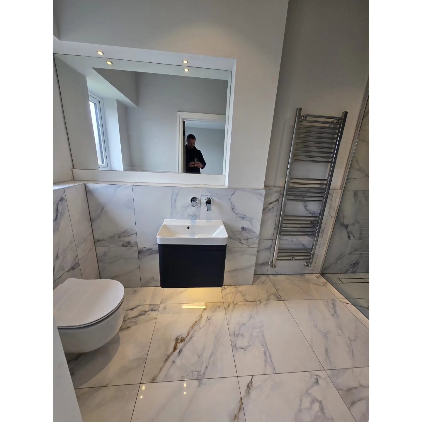 Completed marble bathroom with wall-hung vanity, toilet and illuminated mirror