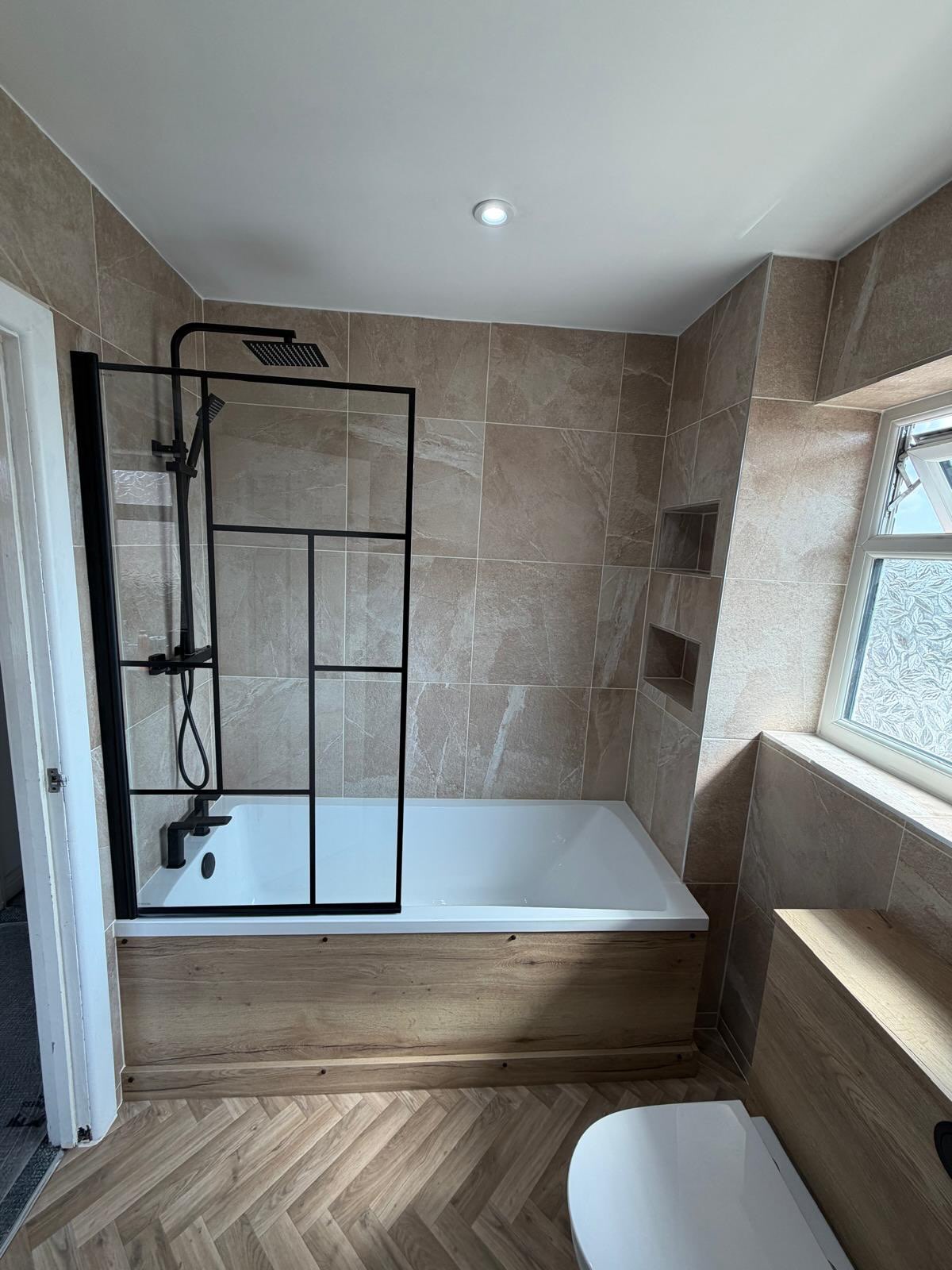 Completed warm stone bathroom with bath, black shower screen and oak finishes